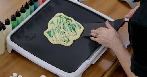 Bulbasaur pancake art step 8.2: When the pancake has cooked through, bubbles will appear and pop on the back, and the batter will no longer appear shiny. At this point, you can begin working your spatula under the pancake around the edges, to gently 'release' it from the griddle.