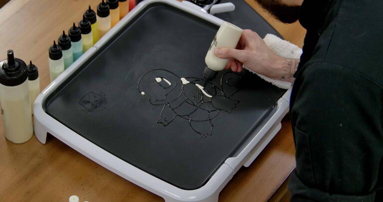 Squirtle Pancake Art step 2.1: Using your white batter, add a shine to each of Squirtle's eyes, as well as the white edge of the larger one. As long as you're holding your white batter, go ahead and color in the edge of Squirtle's shell.