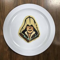 An image of a pancake drawn in the shape of Ezio, protagonist from the Assassin's Creed video game series.