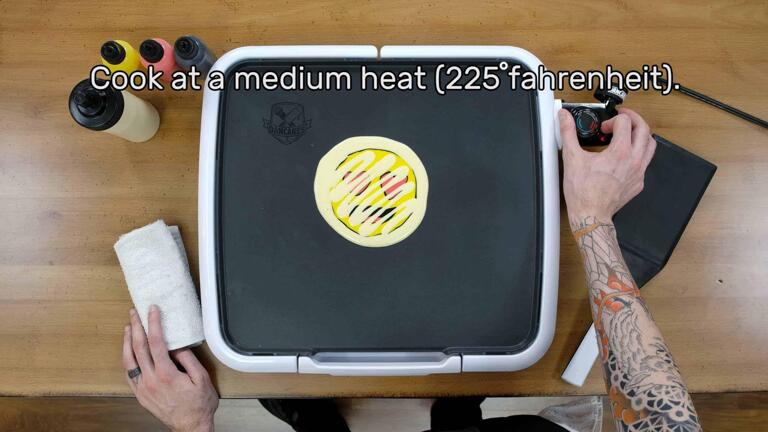 An image that shows the artist adjusting the griddle thermostat to 225 degrees fahrenheit, which is labelled as 'Cook' on the dancakes griddle. The image reads "Cook at a medium heat (225 degrees fahrenheit)."