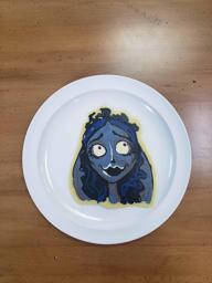 Pancake art of Emily from Corpse Bride, looking disarmingly above and to the right. Her hair is dark blue and her fae and veil are a cool grey.
