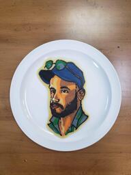 Pancake art of a white man with dark brown beard, an open-collared turquoise button-up shirt, and a blue baseball cap atop which sits a pair of green sunglasses. He is gazing off into the distance at a 3/4 turn from the viewer.